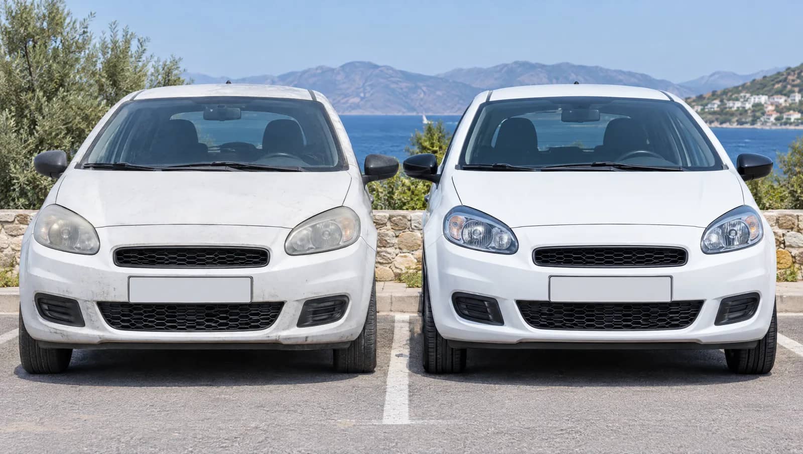 Δύο ολόιδια λευκά αυτοκίνητα σταθμευμένα δίπλα δίπλα με κενές πινακίδες· το αριστερό σκονισμένο και παλιότερο, το δεξί γυαλισμένο, με θάλασσα και βουνά στο βάθος